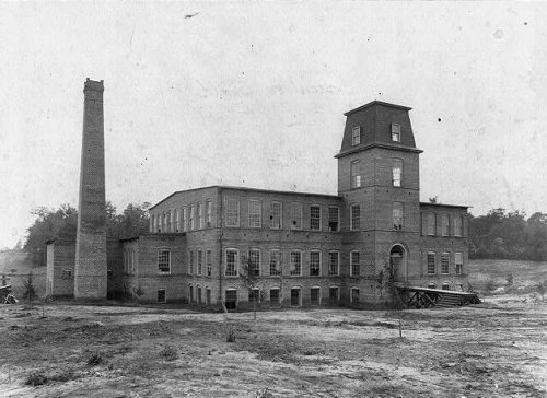 A black and white 19th century photo of a three story brick building in a field