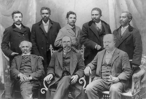 A black and white 19th century photograph of eight businessmen wearing suits