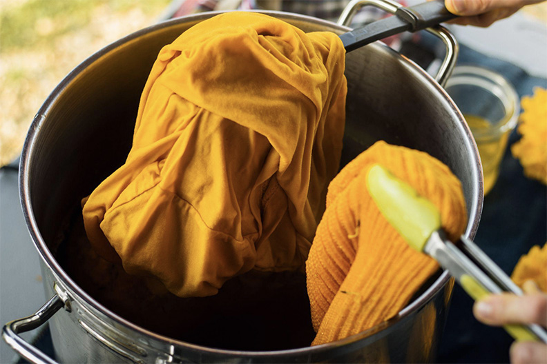Image of beanie and tshirt being dipped in marigold dye and coming out a beautiful gold color,